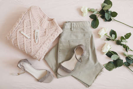 Jeans, knitted sweater, shoes and flowers lie on beige background. Overhead view of womans casual outfit. Trendy stylish women clothes. Flat lay, top view.の写真素材