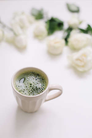 A cup of green tea with white roses on white background view from above. Flatlay, top view, copy spaceの写真素材