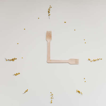 wood fork as clock hands, bamboo cutlery and mimosa flowers on white background, lunch time...