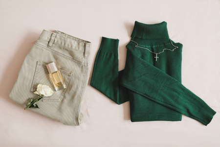 Overhead view of womens casual day outfit. Jeans, green knitted sweater, perfume and accessories on...