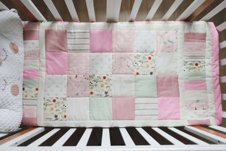 Cozy baby cot with pink patchwork blanket. Baby bedding. Bedding and textile for nursery. Nap and...