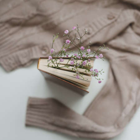 Warm knitted sweater and a book with flowers at white background. Cozy vintage. Flat lay, top viewの写真素材