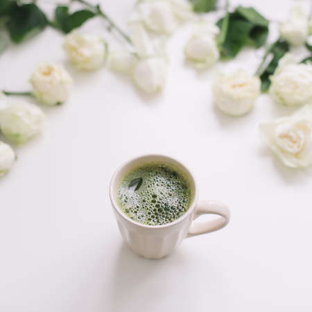 A cup of green matcha tea with white roses on white background view from above. Flatlay, top view, copy spaceの写真素材