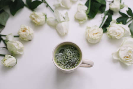 A cup of green matcha tea with white roses on white background view from above. Flatlay, top view, copy spaceの写真素材