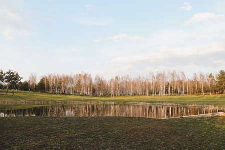 spring landscape, forest lake in spring surrounded by trees, calm water surface with reflection, bright sunlight and blue sky.の写真素材