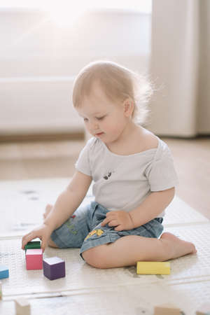 Little girl playing with colorful wooden brickes on the floor in the kids roomの写真素材