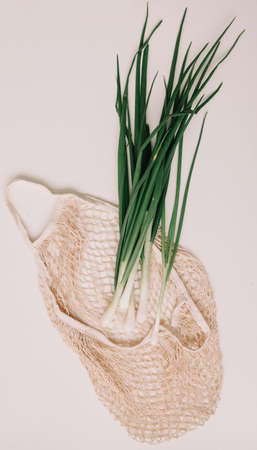 Young green onions on white background. Zero waste shopping concept. Fresh scallion in eco friendly bag on white table top view, flat lay. Healthy organic foodの写真素材