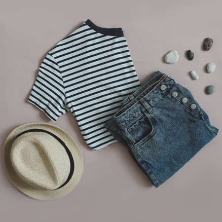 Top view of female casual trendy summer outfit with denim shorts, striped top and straw hat,...
