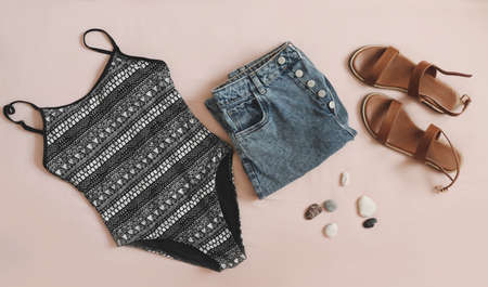 flat lay composition with female swimsuit, denim shorts and sandals on beige background top view