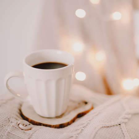a cup of coffee on a knitted beige plaid with bokeh lightsの写真素材