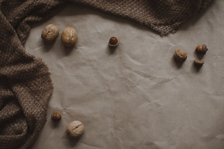 autumn theme, brown paper texture background with cozy warm plaid, walnuts and acorns, top view,...