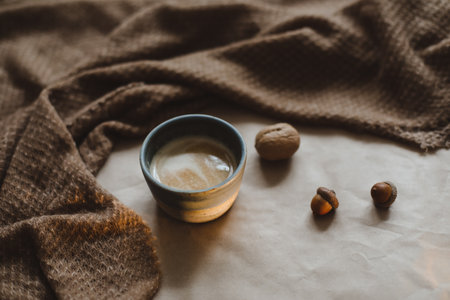 Cup of cappuccino on a brown paper texture background with cozy warm plaid, walnuts and acornsの写真素材