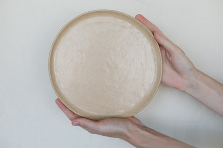 Hands holding ceramic plates isolated on white background. Minimalist set of handmade ceramic...