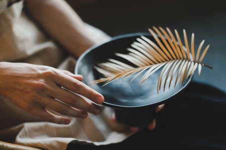 female hands holding a black ceramic plate decorated with fern leaf close-up