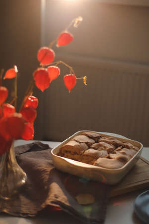 Cozy home breakfast with apple pie, bouquet of red flowers on a table in a sunny roomの写真素材