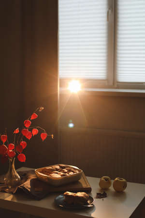 Cozy home breakfast with apple pie, bouquet of red flowers on a table in a sunny roomの写真素材