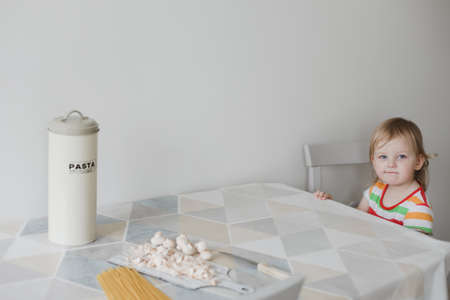 funny little girl sitting in the kitchen waiting for dinnerの写真素材