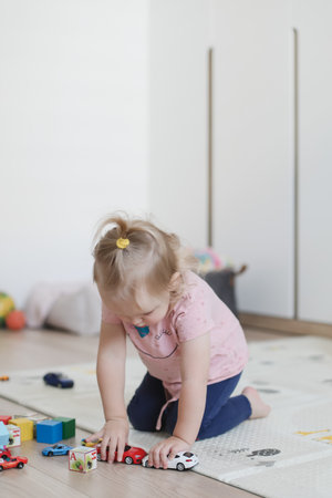 a little funny girl plays with cubes and toys on the floor in the nursery.の写真素材