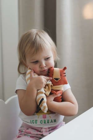 Little baby girl playing with funny small tiger toy, symbol of new 2022 in a sunny nurseryの写真素材