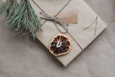 a christmas gift wrapped in craft paper decorated with a dried orange slice and a pine branchの写真素材