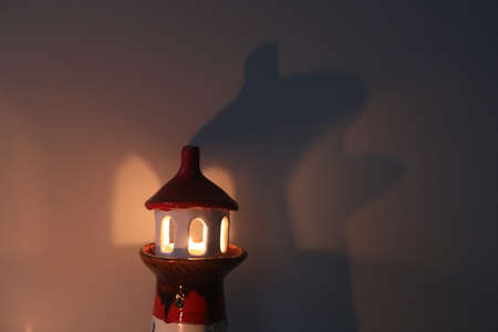 burning candle in a candlestick in the shape of a lighthouse with a shadow, cozy warm atmosphereの写真素材