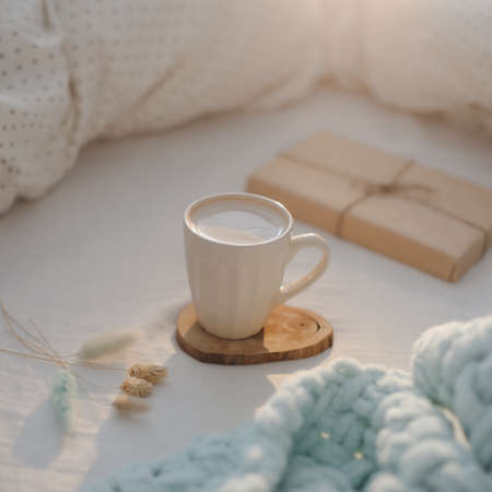 Cup of coffee and a gift on the bed with white linens and blanket. Morning coffee in bed concept.