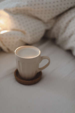 Cup of coffee with milk on the bed with white linens and blanket. Morning coffee in bed concept.の写真素材