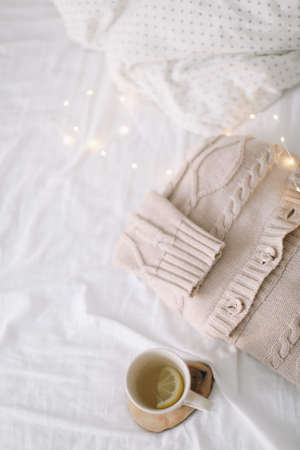 Knitted beige sweater and cup of tea on messy bed background. Winter and spring fashion concept. Top view flat lay.の写真素材