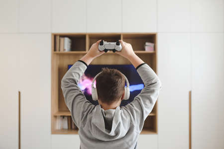 Boy in headphones watching television, teenager boy playing video game in front of screen at homeの写真素材