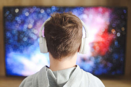 Boy in headphones watching television, teenager boy playing video game in front of screen at homeの写真素材
