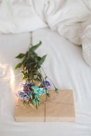 Bouquet of flowers and a gift covered in paper on crumpled white bed sheets.の写真素材