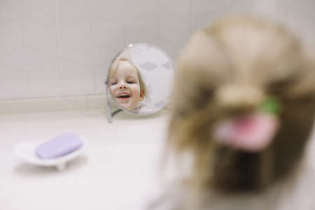 little funny girl brushing teeth and washing hands in the bathroom, reflection in the mirror