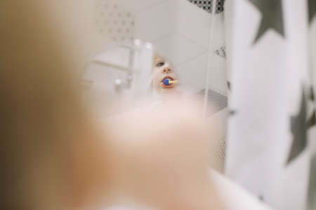 little funny girl brushing teeth and washing hands in the bathroom, reflection in the mirrorの写真素材