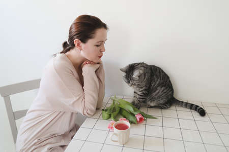 young woman and her cat smelling fresh pink tulips in the morning at homeの写真素材