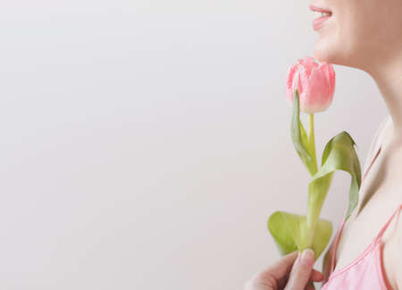spring portrait of a young woman with pink fresh tulip on white background with copyspace.の写真素材