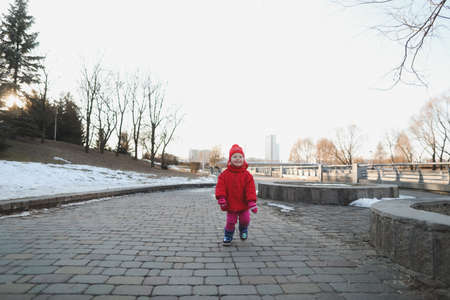 happy baby girl in boots and red jacket. funny cheerful toddler girl playing outdoorsの写真素材
