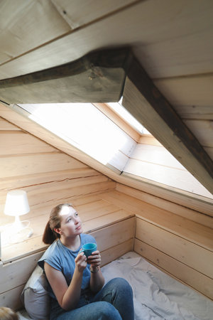 Young woman drinking tea or coffee in bed and looking out the window in the morning at home