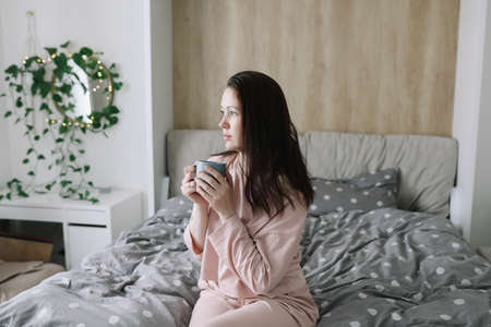 Positive woman with pillow sitting in bed at home. Sweet dreams and good morning conceptの写真素材