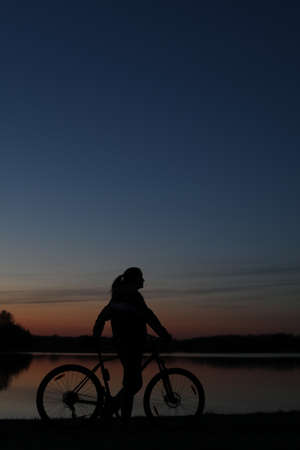 Silhouette of woman with mountain bike on colorful blue sky sunset background. Active outdoors lifestyleの写真素材