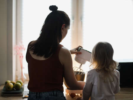 little girl helping her mother cooking in the kitchen