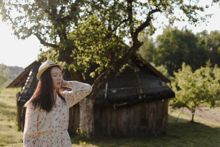 romantic portrait of a young woman in straw hat and beautiful dress in the countryside in summer
