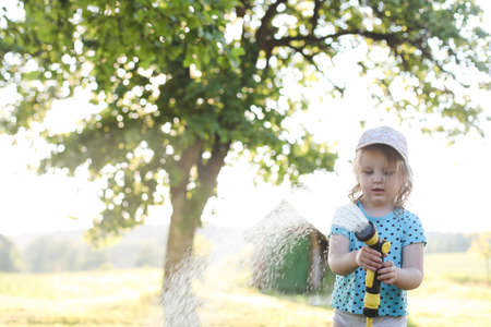 Adorable little girl playing with a garden hose on hot and sunny summer dayの写真素材