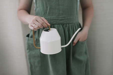 Girl in apron holds a watering can. Watering and caring for home plants. home gardening. hobby flower cultivationの写真素材