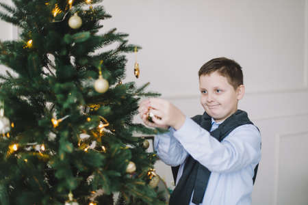 smiling caucasian child boy decorating Christmas tree in a home interior and festive atmosphere