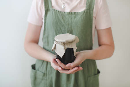 Woman housewife in apron holding a glass jar of sweet homemade jam, close-upの写真素材