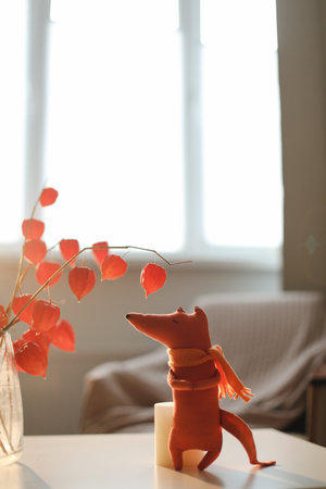 autumn still life with a toy fox, flowers, twigs of red physalis in a vase in a cozy home interiorの写真素材