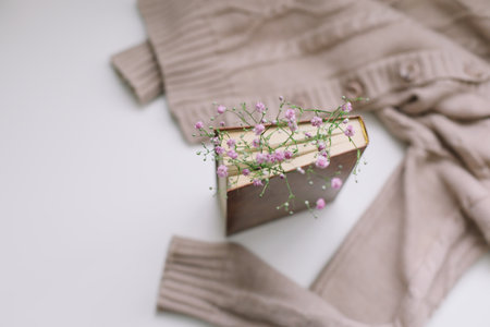 Warm knitted sweater and a book with flowers at white background. Cozy vintage. Flat lay, top view