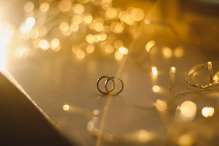 Wedding rings on blured bokeh glowing golden background. Symbol of love and romance on a textured...