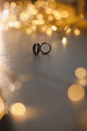 Wedding rings on blured bokeh glowing golden background. Symbol of love and romance on a textured...