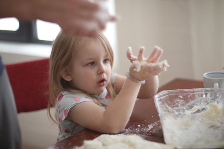 little girl helps to cook by kneading the dough, a child helps to cook at home. Homemade food and little helper.の写真素材